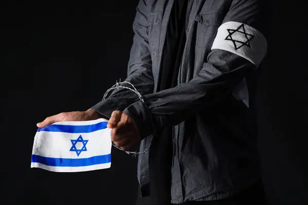 Young Jewish man with barbed wire and flag of Israel on black background, closeup. International Holocaust Remembrance Day