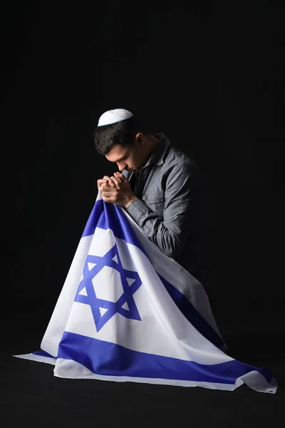Young Jewish man with flag of Israel praying on black background. International Holocaust Remembrance Day