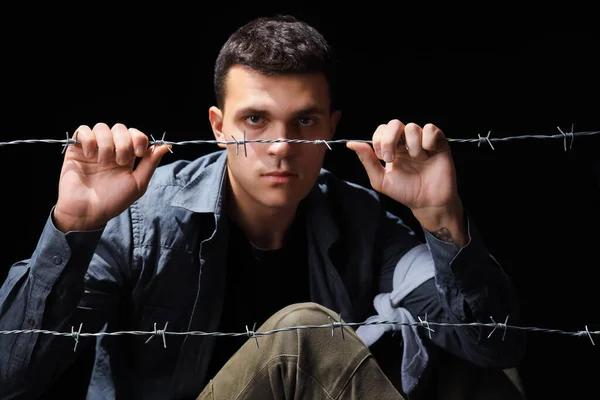 Young Jewish man behind barbed wire on black background. International Holocaust Remembrance Day