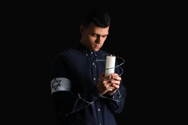 Young Jewish man with barbed wire and burning candle on black background. International Holocaust Remembrance Day
