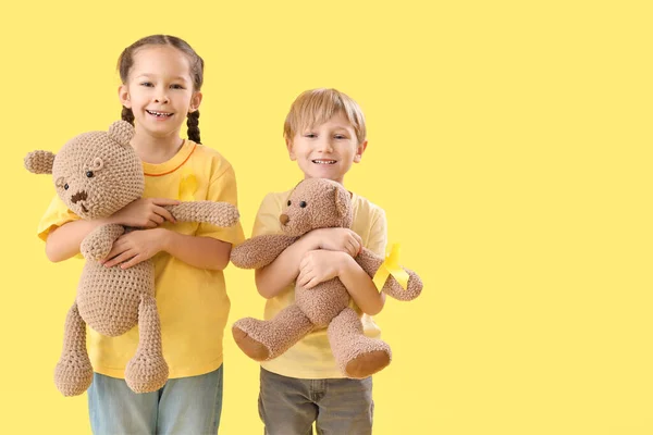 Cute little children with yellow ribbons and teddy bears on color background. Childhood cancer awareness concept
