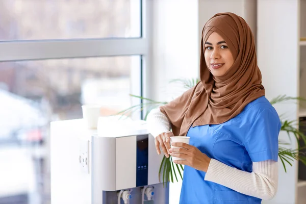 Pasante Médica Musulmana Con Taza Agua Cerca Del Refrigerador Clínica —  Fotos de Stock