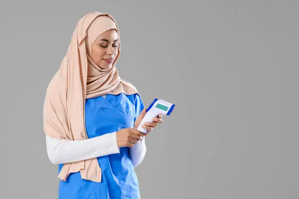 Pasante Médica Musulmana Femenina Con Termómetro Infrarrojo Sobre Fondo Claro —  Fotos de Stock