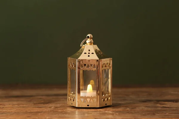 Silver Muslim lamp with burning candle for Ramadan on wooden table against dark green background