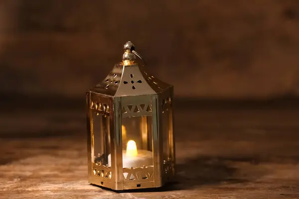Silver Muslim lamp with burning candle for Ramadan on wooden table, closeup