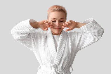 Bornozlu genç bir kadın arka planda yüz masajı yapıyor.