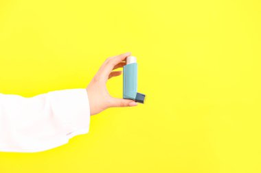 Sarı arka planda astım spreyi olan kadın doktor.