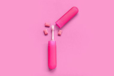 Diş fırçası ve pembe arka planda diş eti çiğneyen bir kap.