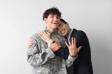 Genç asker ve kocası hafif arka planda sarılıyorlar.