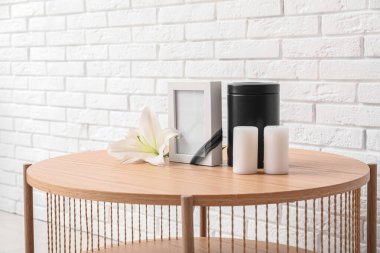 Boş cenaze çerçevesi, morg vazosu, mumlar ve nilüfer çiçekleri açık tuğla duvarın yanındaki ahşap masada.