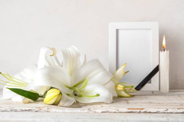 Güzel zambak çiçeği ve boş cenaze çerçevesi masanın üstünde.