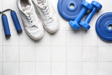 Halter plakaları, ayakkabılar, atlama halatı ve beyaz fayanslı halterler.