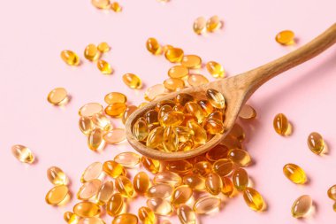 Ahşap kaşık ve pembe arka planda balık yağı hapları.