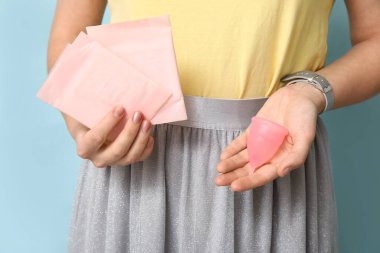 Adet pedleri ve mavi arka planda fincanı olan genç bir kadın, yakın plan.