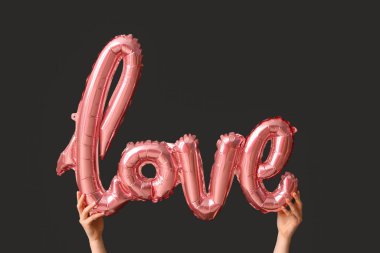 Siyah arka planda kelime şeklinde balonu olan bir kadın. Sevgililer Günü kutlaması