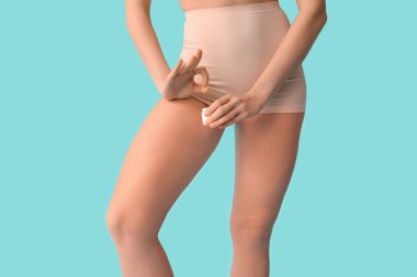 Bir kavanoz anti-selülit kremi olan güzel genç bir kadın mavi arka planda iyi bir jest gösteriyor.