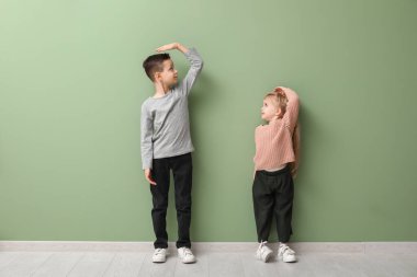 Yeşil duvarın yanında boyunu ölçen sevimli küçük çocuklar.