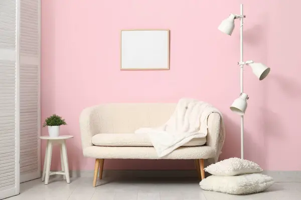 Cozy white sofa, pillows and lamp near pink wall