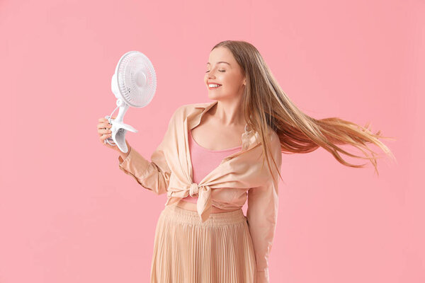 Молодая женщина с электрическим вентилятором на розовом фоне