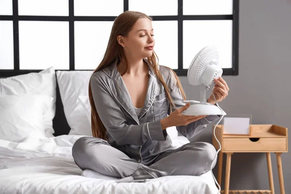 Young woman with electric fan in bedroom