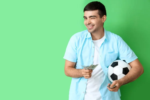 Happy young man with soccer ball and money on green background. Sports bet concept