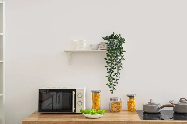 Shelf with plant and cups on light wall in kitchen