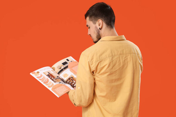 Young man reading magazine on orange background, back view