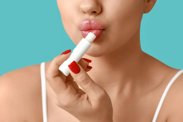 Young woman applying lip balm on color background, closeup