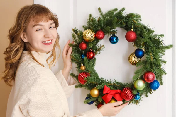 Woman in white sweater hanging Christmas wreath on door