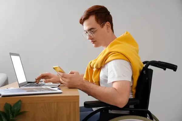 Young man in wheelchair working with laptop at office