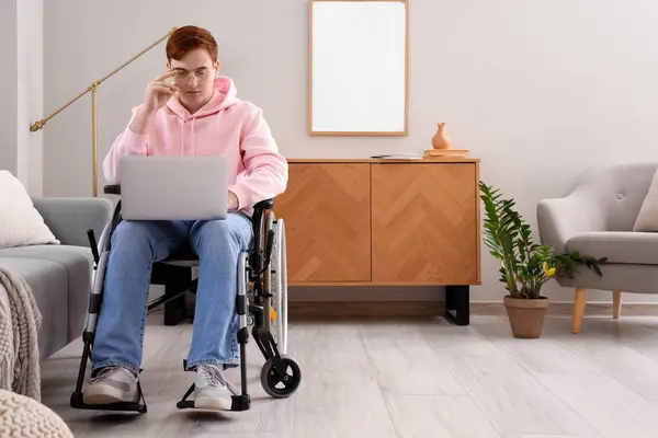 Young man in wheelchair using laptop at home