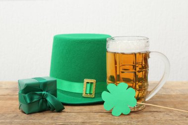 Leprikon şapkalı bir kupa, hediye kutusu ve beyaz arka planda tahta masa üzerinde kağıt yonca. Aziz Patrick Günü kutlaması