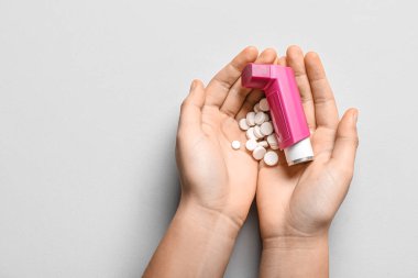 Astım spreyli çocuk elleri ve beyaz arka planda haplar.