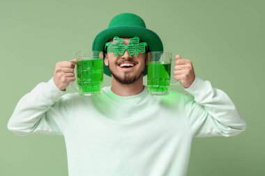 Yeşil arka planda bira kupaları olan cüce şapkalı mutlu genç adam. Aziz Patrick Günü kutlaması