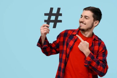 Yakışıklı genç adam mavi arkaplandaki etiket işaretine işaret ediyor