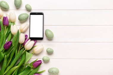 Modern cep telefonlu kompozisyon, güzel lale çiçekleri ve hafif ahşap arka planda Paskalya yumurtaları.