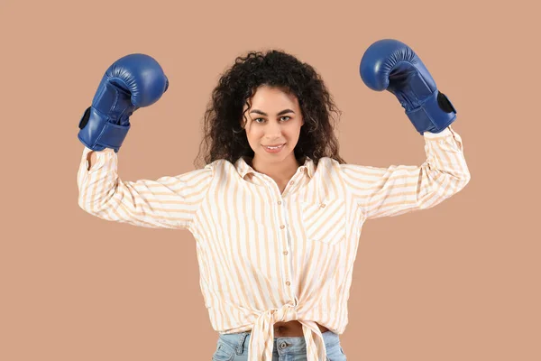 Beautiful young happy African-American woman in boxing gloves on beige background. Women history month