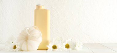 Bir şişe kozmetik ürünü, banyo süngeri ve açık arkaplanda papatya çiçeği. Tasarım için pankart