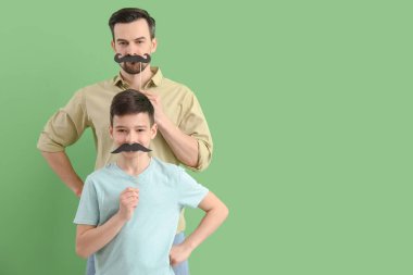 Yeşil arka planda kağıt bıyıklı babasının ve küçük oğlunun portresi.