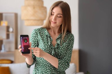 Akıllı ev güvenlik kontrol paneli olan cep telefonu kullanan genç bir kadın.