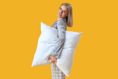 Pijamalı ve sarı arka planda yastığı olan mutlu genç bir kadın.