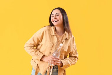 Sarı arka planda bir şişe suyu olan genç bir kadın.