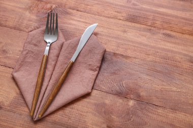Kahverengi ahşap arka planda peçeteli modern gümüş çatal bıçak.