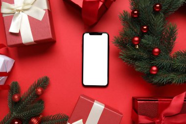 Modern cep telefonlu kompozisyon, Noel hediyeleri ve kırmızı arka planda süslemeler, yakın plan