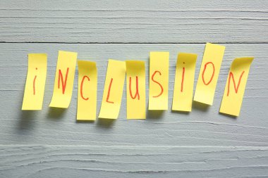 Gri ahşap arka planda kelime INCLUSION kağıt parçaları