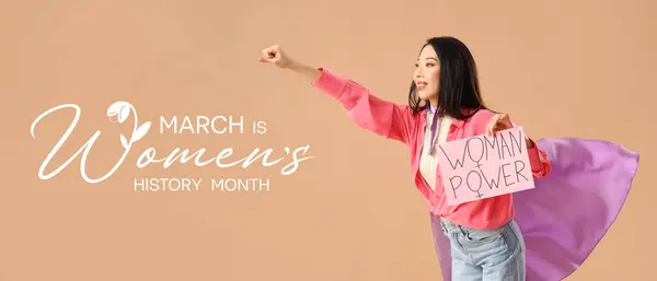 Young Asian girl dressed as superhero holding paper with text WOMAN POWER on beige background. Banner for Women's History Month
