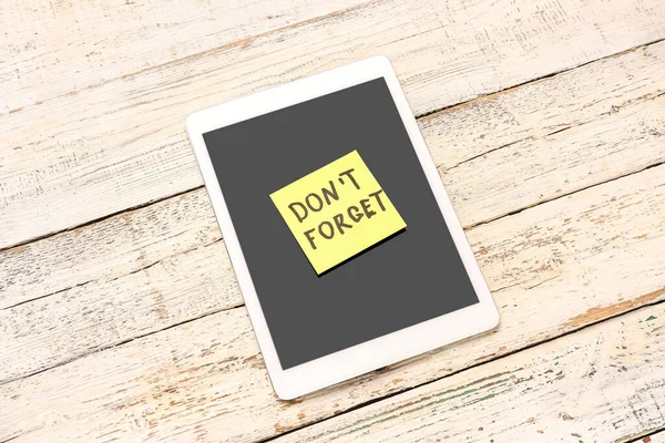 Sticky note with text DON\'T FORGET and tablet computer on white wooden background