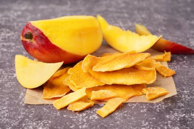 Koyu masa üzerinde kurutulmuş mango dilimleri olan kağıt fırını.