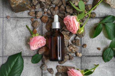 Gül özlü bir şişe kozmetik yağı, gri fayansların üzerinde çiçekler ve yapraklar