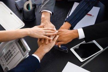 Bir grup iş adamı toplantı salonundaki masada el ele tutuşuyorlar.